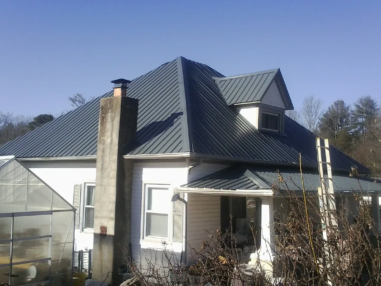 Dark blue standing seam metal roof on a white farmhouse with dormer — Slate & Tile Roof Repair by Roofing Brothers in Casselton