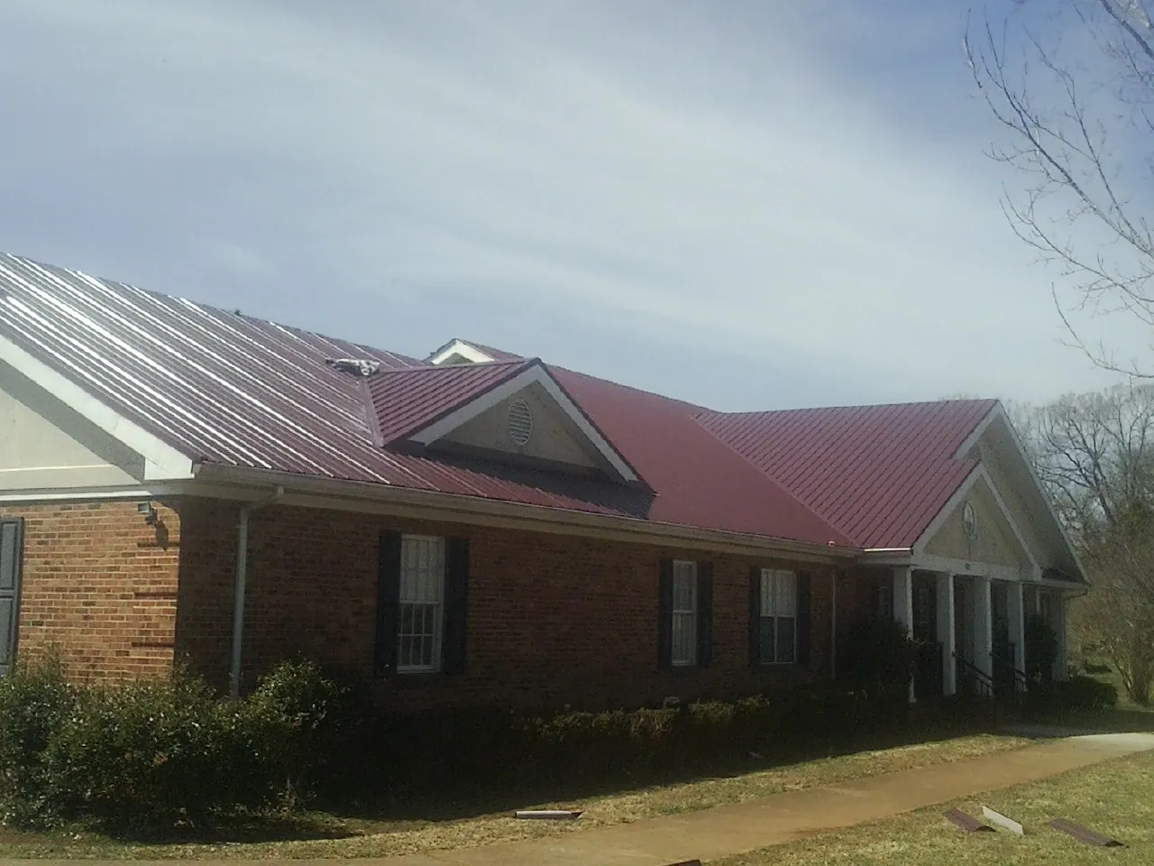 Red metal roof with gabled entries on a long brick building, from a Hail Damage Roof Repair job in Casselton