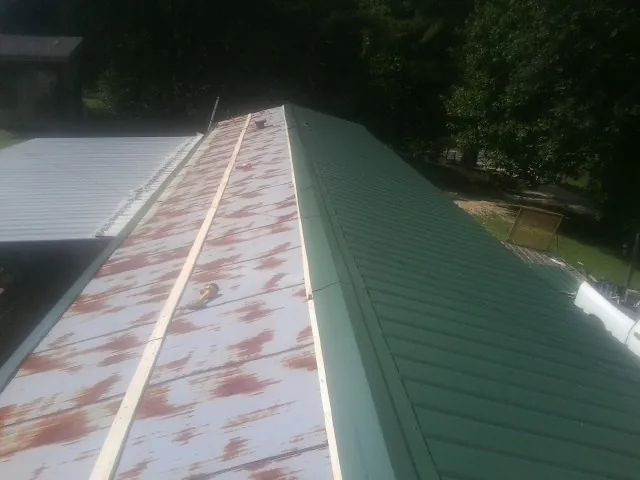 Old rusted panels beside newly installed green metal roofing — Wind Damage Roof Repair by Roofing Brothers in Casselton
