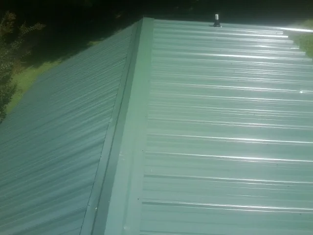 New green metal panels meeting at the ridge of a roof — Flat Roof Repair work by our crew in Casselton