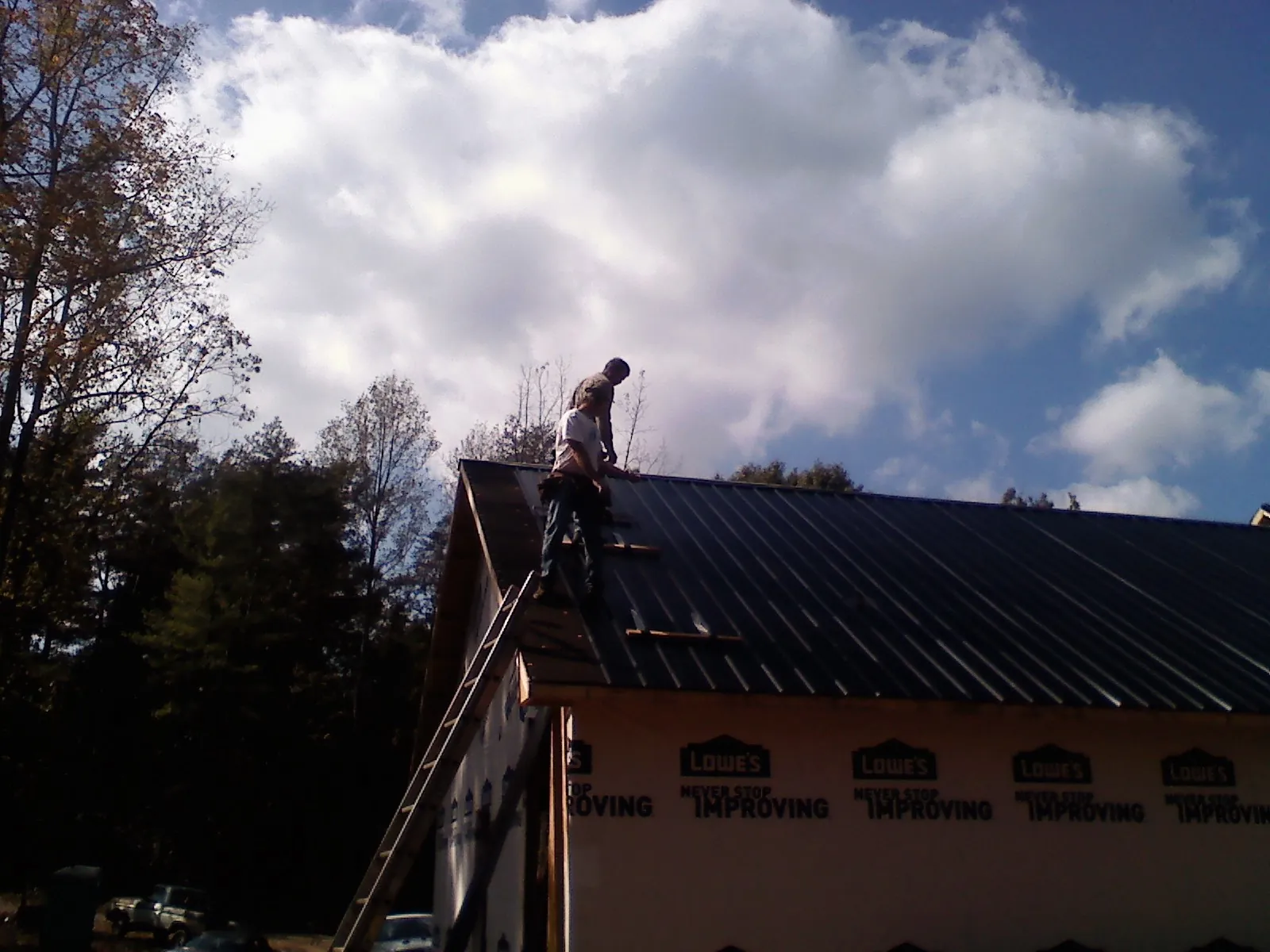 Roofer fastening dark metal panels high against a cloudy sky, from a Roof Inspection job in Casselton